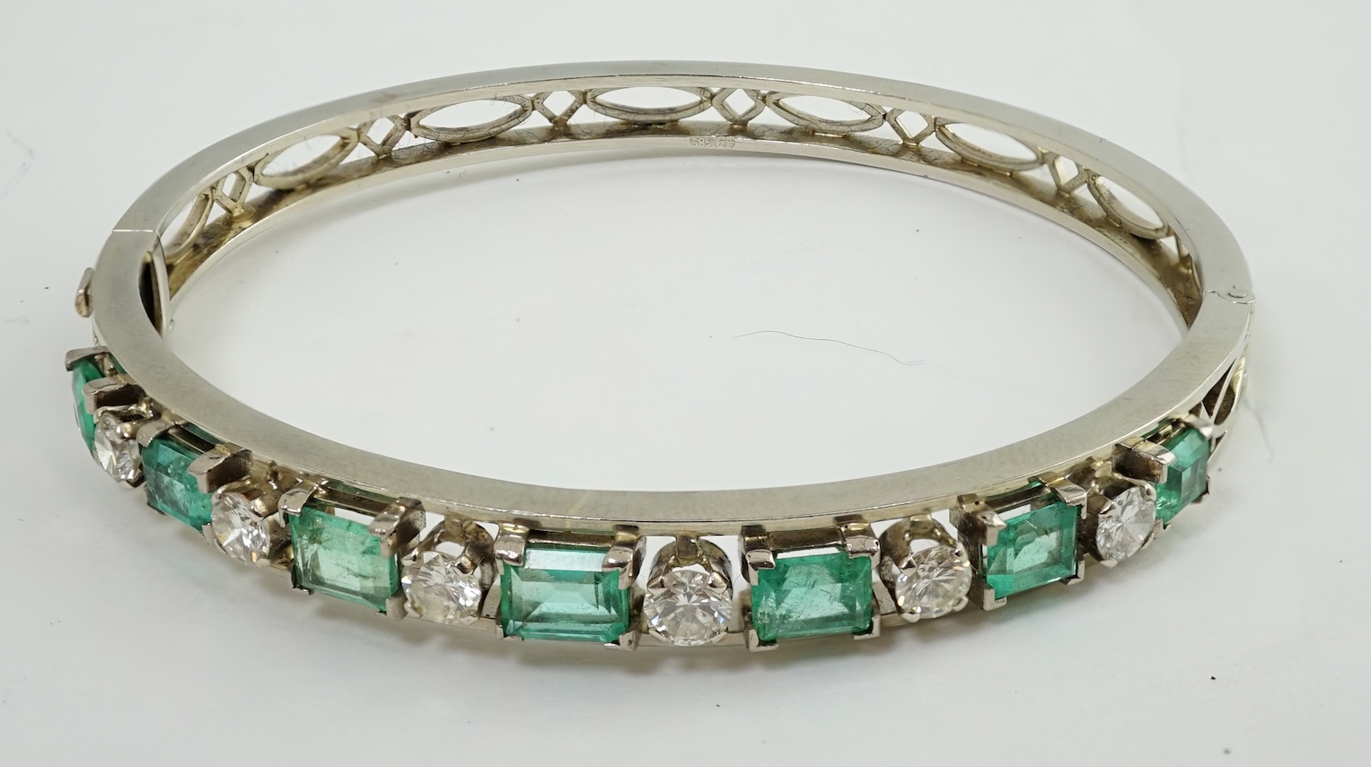 A modern 14k white gold, seven stone graduated emerald and six stone round cut diamond set hinged bangle